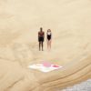 chico y chica caminando por la playa hacia toallas de playa estiradas sobre la arena
